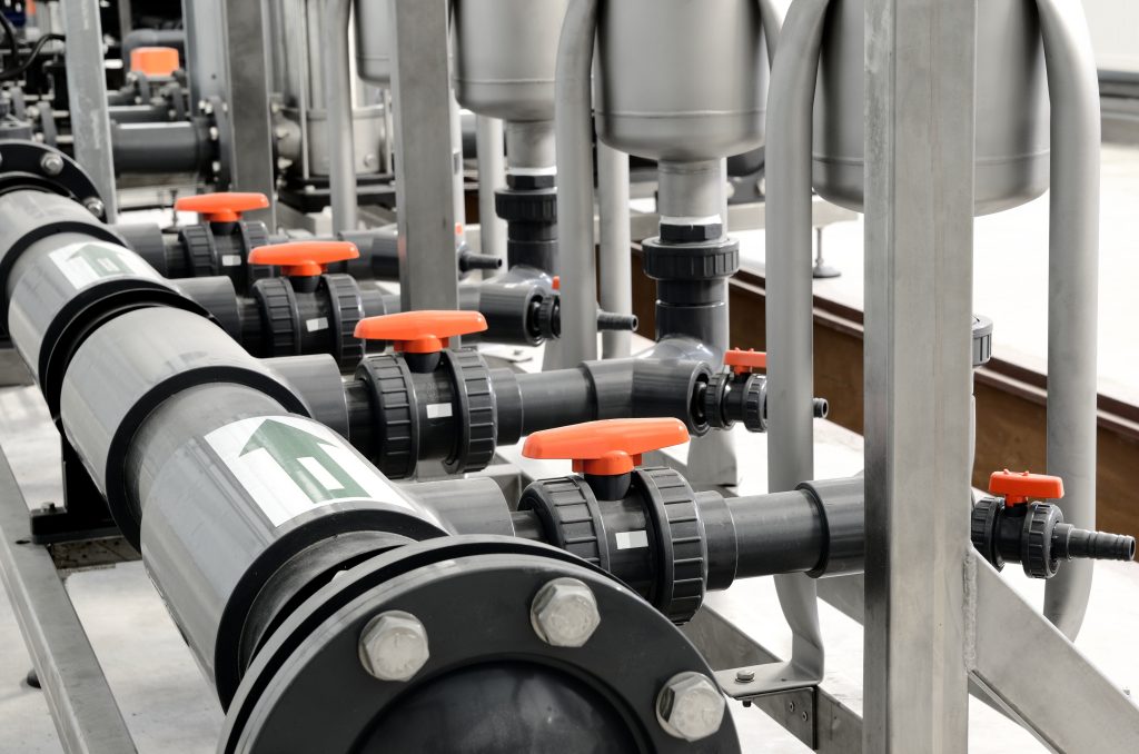 Pool filtration equipment connected by plastic pipework, flanged fittings and orange-handled valves.