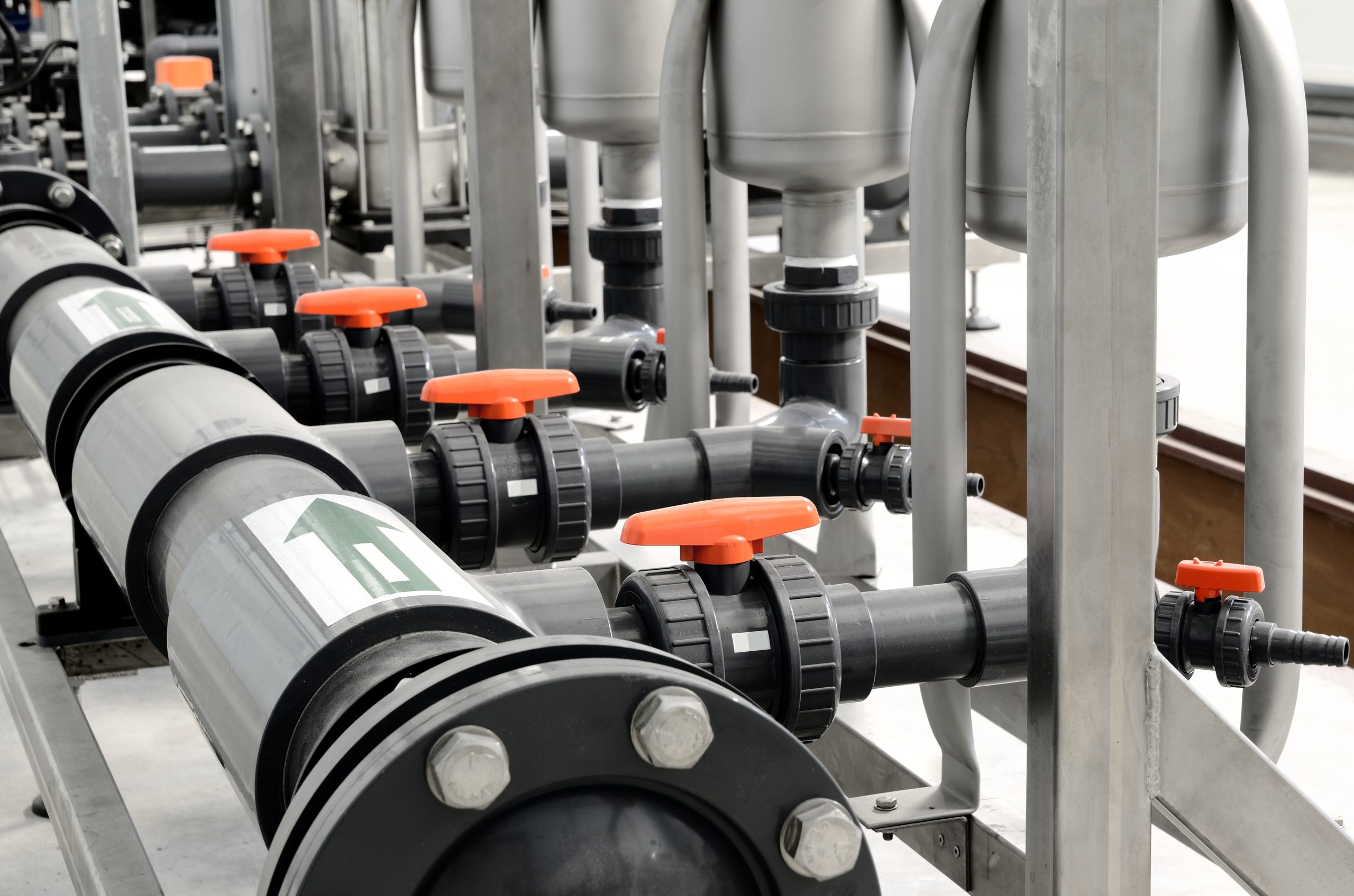 Pool filtration equipment connected by plastic pipework, flanged fittings and orange-handled valves.